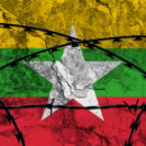 The national flag of myanmar (burma) painted on a grungy wall with barbed wire in the foreground. concept of the shut down in myanmar after the military coup.