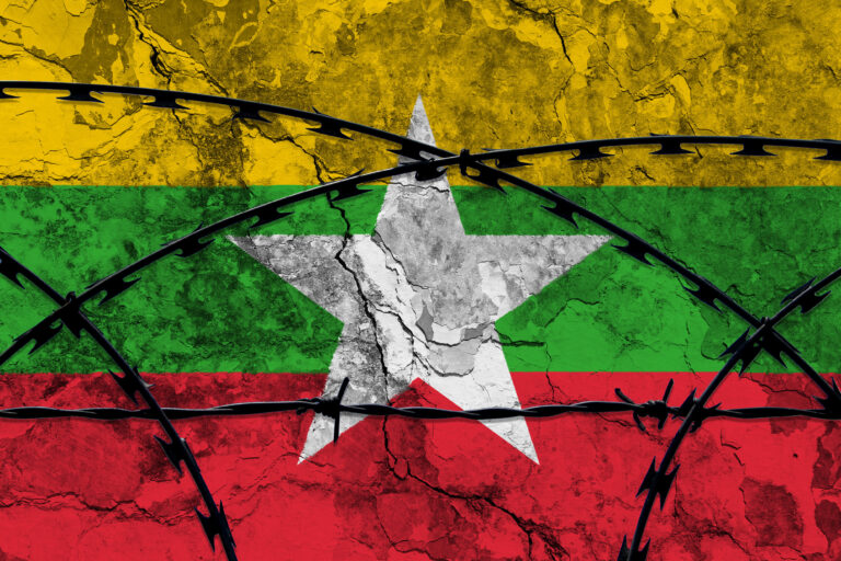 The national flag of myanmar (burma) painted on a grungy wall with barbed wire in the foreground. concept of the shut down in myanmar after the military coup.